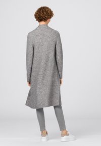 Long, grey cardigan made of soft knit material, featuring a straight cut, high neck, and side slits, paired with slim-fit grey jeans and white sneakers.