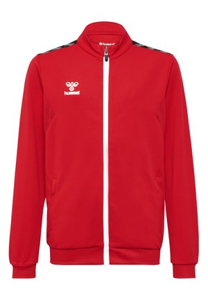 Rote Trainingsjacke mit strukturiertem Finish, weißem Reißverschluss, Seitentaschen und schwarzem Chevron-Muster entlang der Schultern. Hummel-Logo in Weiß.