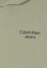 Světlé zelené mikinové triko s texturovanou látkou a přední kapsou ve stylu klokánka. Nese logo "Calvin Klein Jeans" vyšívané černou nití.