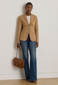 Bēša žakete ar zelta pogu un ģerboņa detaļu, kombinēta ar izplatītām džinsa biksēm. Brūna somiņa ar ķēdes siksniņu noslēdz tērpu.