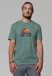 Groen katoenen t-shirt met een cartoonafbeelding van een fietser in levendig oranje en rood op een fiets met zwarte wielen. Korte mouwen, ronde hals.