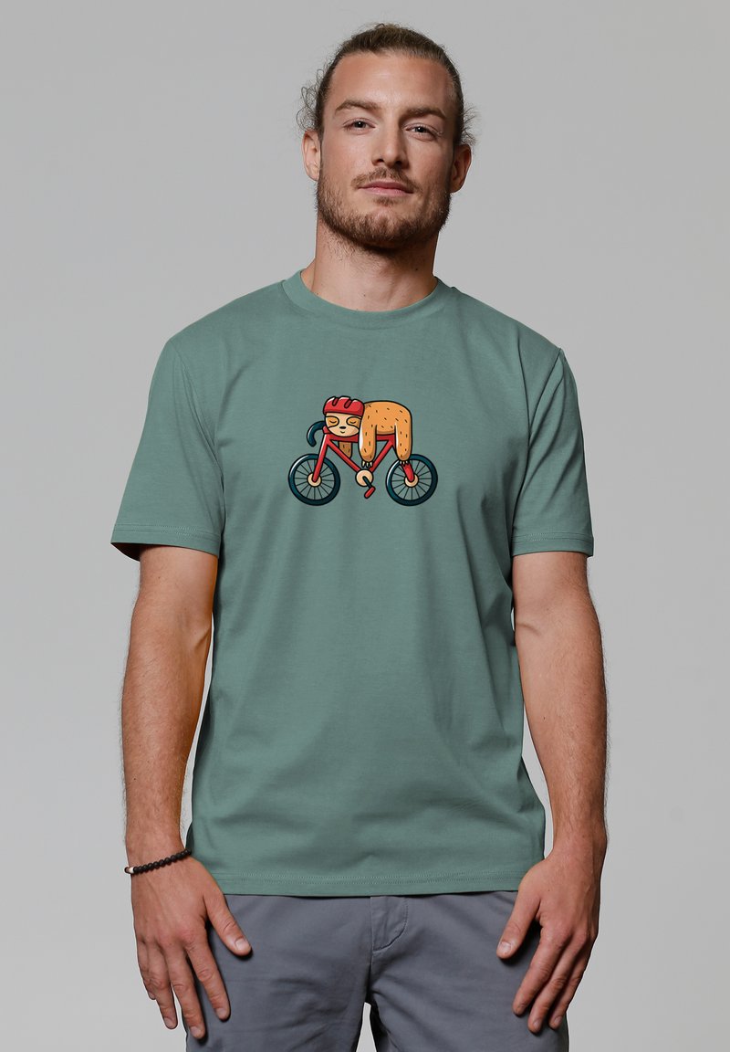 Groen katoenen t-shirt met een cartoonafbeelding van een fietser in levendig oranje en rood op een fiets met zwarte wielen. Korte mouwen, ronde hals.