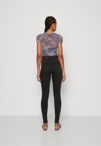 Lettvekts, tettsittende topp i tie-dye nyanser av lilla og grå, sammen med høyhåndde mørke denimjeans og flate sandaler, sett fra bak.