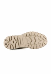 Suola di scarpa in gomma beige con scanalature profonde, motivi a zig-zag e piccoli fori vicino alla punta, isolata su sfondo bianco.