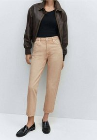 Veste aviateur en cuir marron, haut côtelé noir, jean taille haute beige clair et mocassins noirs. Tenue décontractée avec un contraste de couleurs distinct.