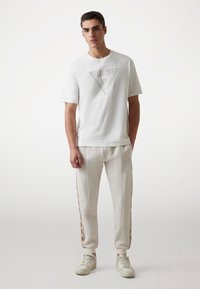Hvid bomulds T-shirt med et trekantet logo-grafik, parret med lyse svedbuks med sidelommer og ribkant ved anklerne.
