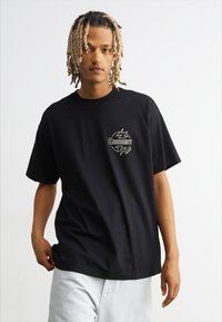 Camiseta de algodón negra con mangas cortas, que presenta un diseño de logo en contraste en el pecho. Corte relajado y cuello redondo.