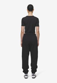 Zwarte katoenen cropped top met korte mouwen, gecombineerd met zwarte katoenen joggers met een elastische tailleband en gathered manchetten, gedragen met witte sneakers.