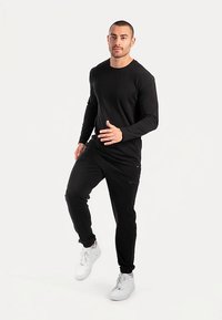 Sort langærmet skjorte parret med sorte joggerbukser. Stoffet ser glat ud med et figursyet design. Hvide sneakers fuldender outfittet.