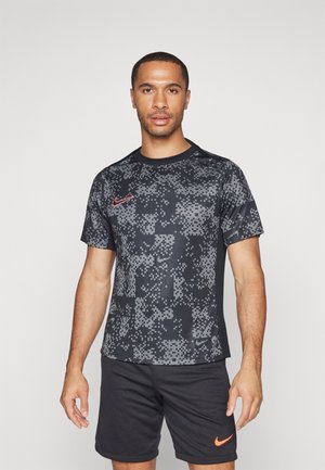 T-shirt de sport noir à manches courtes avec un motif gris pixelisé, arborant un logo Nike rouge sur la poitrine ; tissu lisse et léger.