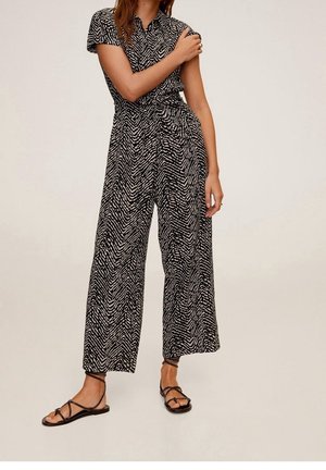 Czarnobiały kombinezon w wzory z krótkim rękawem, taliowany, z szerokimi nogawkami, zestawiony z czarnymi sandałami na paski.