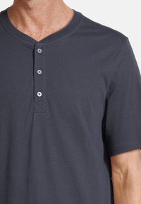 Maglietta henley grigio scuro con scollatura arrotondata, patta con tre bottoni, maniche corte e una texture morbida e liscia.