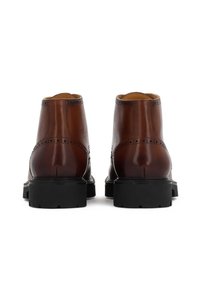 Stivali alla caviglia in pelle marrone con dettagli brogue, punta tonda e una robusta suola in gomma nera. Texture liscia e finitura lucida.