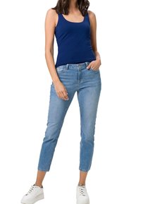 Débardeur marine associé à un jean slim bleu clair, avec une taille mi-haute et des ourlets retroussés, complété par des baskets blanches.