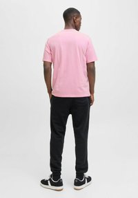 Camiseta de manga corta rosa claro, pantalones jogger negros con puños elásticos y zapatillas negras con acentos blancos, vistas desde la parte de atrás contra un fondo neutro.