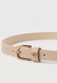 Μπεζ δερμάτινη ζώνη με υφή, με χρυσή πόρπη και διακοσμητικό χρυσό έμβλημα στον βρόχο της ζώνης, τοποθετημένη επίπεδη σε λευκό φόντο.