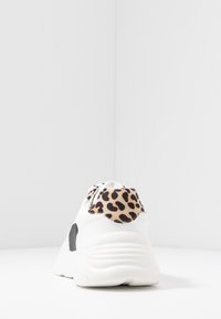 Zapatilla blanca con detalles en negro y una pestaña de talón con estampado de leopardo. Presenta una textura suave y una suela acolchada para mayor comodidad.