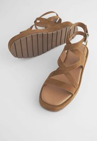 Pruunist nubukist sandaalid, millel on lame tall, ristatud rihmad toe toestamiseks ja metallne pandla. Tekstuuriga tall, millel on horisontaalsed sooned.