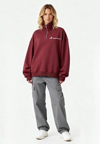 Sweat-shirt bordeaux avec fermeture quart de zip et broderie blanche "Amour" ; associé à un pantalon cargo gris avec poches latérales et poignets élastiques.