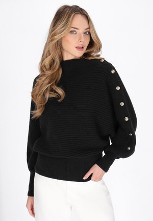 Maglione nero a maglia con colletto alto, texture a coste e bottoni dorati lungo una manica. Vita aderente con maniche a palloncino.