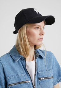 Black cap with a curved brim and white logo, paired with a denim jacket featuring two zippered pockets and a collared design.