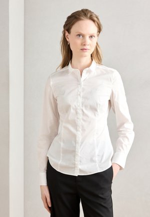 Witte lange mouwen overhemd met een button-down kraag, met een getailleerd ontwerp en subtiele details op de borst, gecombineerd met zwarte broek.