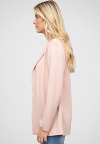 Lys pink, langærmet cardigan med åben frontdesign, der har en blød tekstur og afslappet pasform. Sammen med blå jeans.