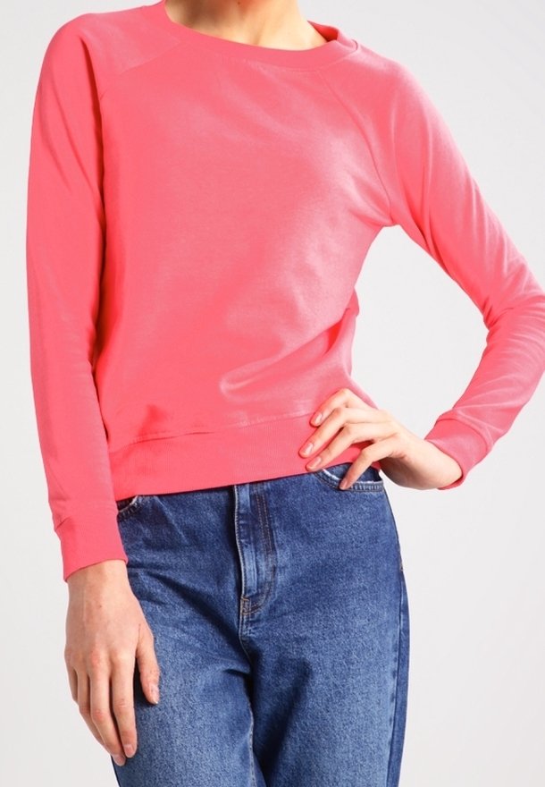 Personne portant une chemise rose vif à manches longues avec un jean en denim bleu, une main sur la hanche et l'autre pendant le long du corps.