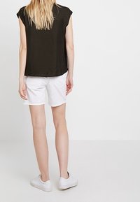 Svart kortärmad topp med en avslappnad passform, tillsammans med vita shorts. Shorts är uppvikta vid fållen och outfiten inkluderar vita sneakers.