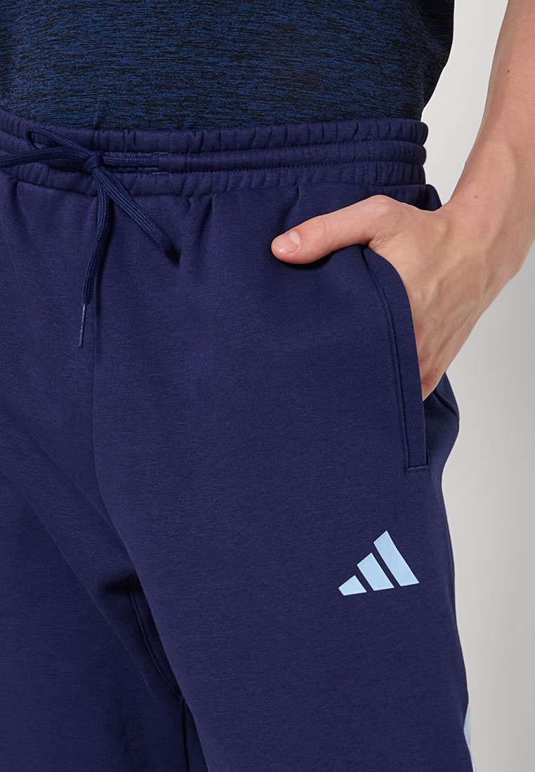 Marineblauwe sweatpants met een trekkoord in de taille, voorzien van zijzakken en een lichtblauw logo met drie strepen op het onderbeen. Zacht materiaal en een relaxte pasvorm.