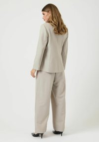 Ljusgrå kostym med en skräddarsydd blazer och vida byxor. Tyget har en subtil textur. Matchas med svarta spetsiga klackar.