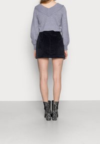 Šedý svetr s výstřihem do V, doplněný černou minisukní z kordurové látky a černými kotníkovými botami s hadím vzorem. Hladká látka a texturovaný design.