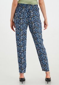 Pantaloni floreali con sfondo blu navy, decorati con fiori blu, verdi e bianchi, vita elastica e gambe affusolate.
