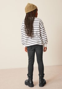 Chemise longue rayée blanche et marine, jeans slim noirs et bottes de combat noires avec boucles, le tout surmonté d'un bonnet en tricot beige.