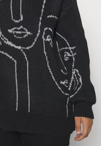 Pull en maille noir avec un dessin en ligne blanche de visages. Coupe ample, bordures côtelées aux poignets et à l'ourlet. Tissu texturé avec des détails en tissage ouvert.