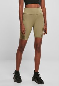 Shorts de cyclisme vert olive en matière lisse et extensible, dotés d'une taille haute et de poches latérales, associés à des bottines noires.