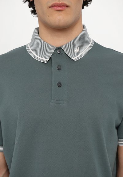 Grønn polo med strukturert stoff, med stripete krage og tre svarte knapper. Liten logo-detalj på kragen.