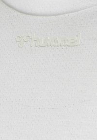 Hvid atletisk skjorte med et tekstureret, åndbart stof og et diskret "hummel" logo i en matchende hvid tone.