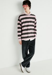 Chemise à rayures à manches longues en rose et gris foncé, associée à un pantalon en velours côtelé noir. Portée avec une chemise blanche en dessous et des baskets grises.