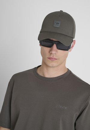 Tamna maslinasta kapa sa kvadratnom logom, crne pravokutne sunčane naočale i tamnosiva majica s kratkim rukavima koja sadrži diskretno brendiranje.