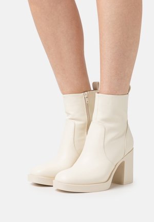 White leather ankle boots with a high block heel, featuring a side zipper and a smooth texture. Designed with a minimalistic aesthetic.
