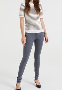 Top blanco de manga corta con rayas horizontales multicolores; jeans ajustados grises; tacones negros de punta. Diseño simple y texturizado.