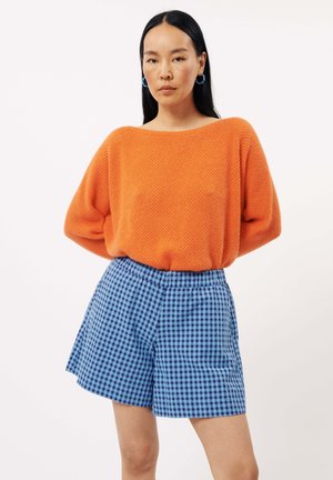 Pull en maille texturé orange associé à un short à carreaux bleu et noir. L'ensemble présente une coupe décontractée et une taille élastique.
