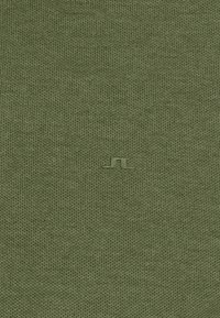 Tissu vert texturé avec un petit logo géométrique embossé centré près du bas.
