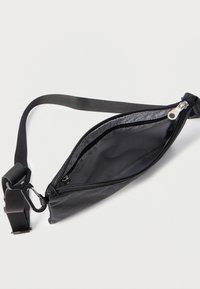 Čierna nylonová crossbody taška s textúrovaným vonkajším povrchom, uzatvárateľná na zips, nastaviteľným popruhom a jedným priehradkovým vnútrom.