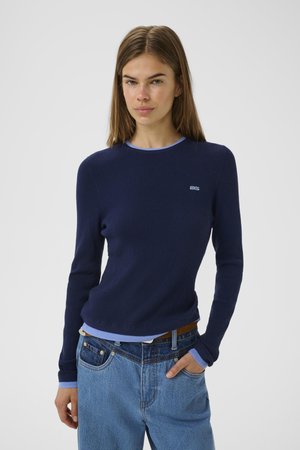 Navy ribbed long-sleeve knit top with light blue collar. Paired with high-waisted blue denim jeans, featuring a brown belt.