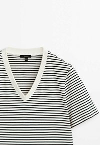 Chemise blanche à manches courtes avec col en V, fines rayures horizontales noires et col blanc uni, pliée à plat sur fond blanc.
