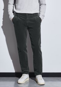 Pantalones de pana verde oscuro con bolsillos laterales, corte recto, combinados con zapatillas blancas. La tela tiene un acabado texturizado.