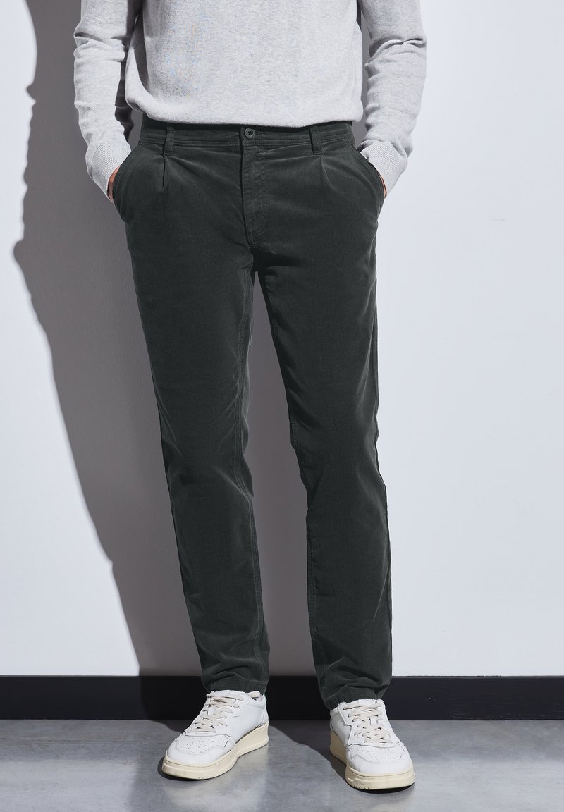 Pantalones de pana verde oscuro con bolsillos laterales, corte recto, combinados con zapatillas blancas. La tela tiene un acabado texturizado.