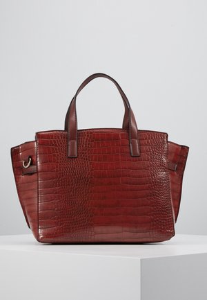 Sac à main en cuir marron avec texture crocodile, deux poignées, et détail anneau métallique sur le côté, présenté sur un piédestal blanc sur fond gris.